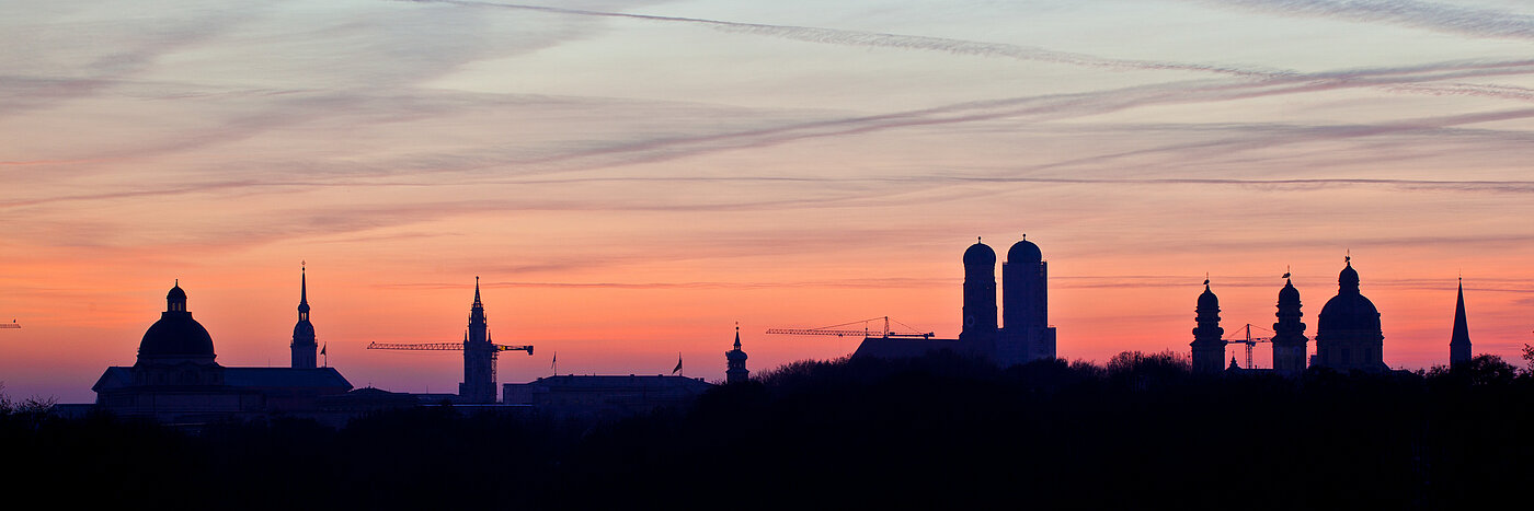 Zu sehen ist die Skyline von München, im Hintergrund ist der rosa eingefärbte Himmel