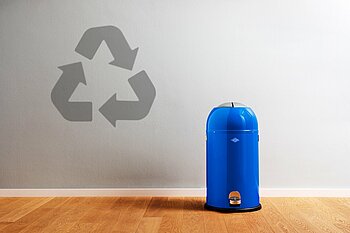 Das Bild zeigt einen blauen Mülleimer rechts, und das Recycling-Symbol zu seiner linken.
