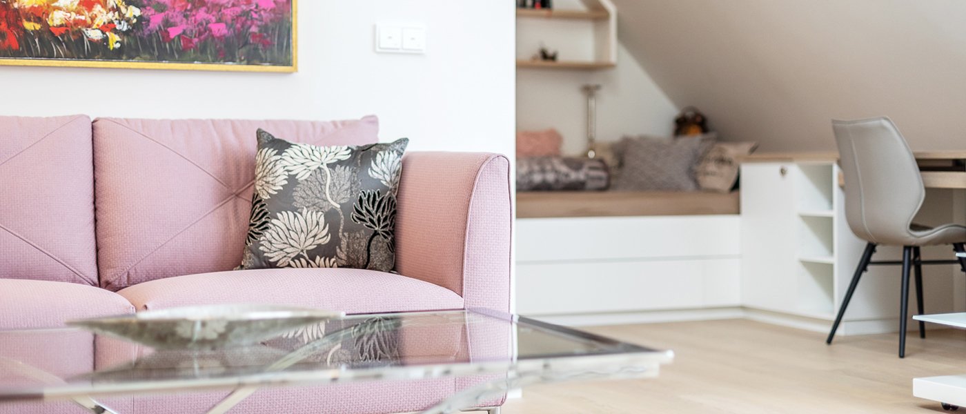 Zu sehen ist ein Sofa im Vordergrund und ein Bett sowie ein Arbeitsplatz im Hintergrund